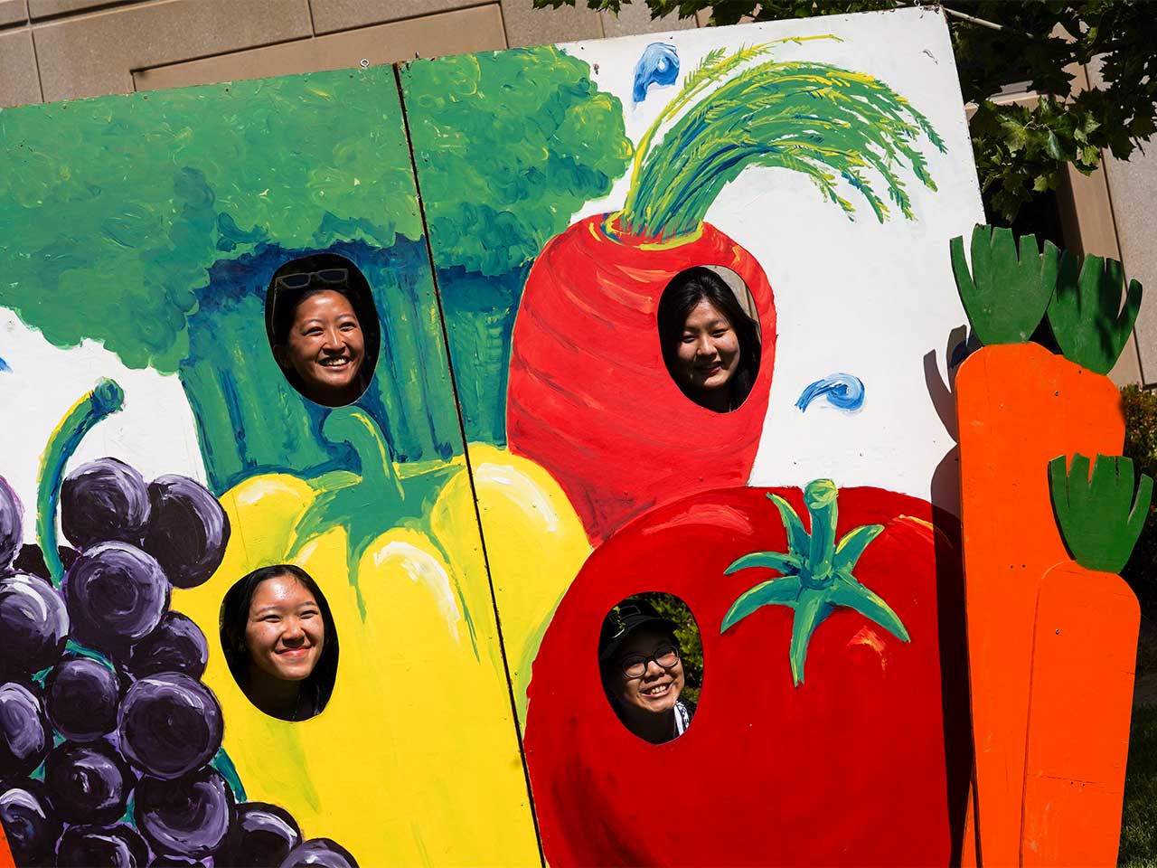 4 students taking a photo at the vegetable photo booth in front of the Plant Sciences building.