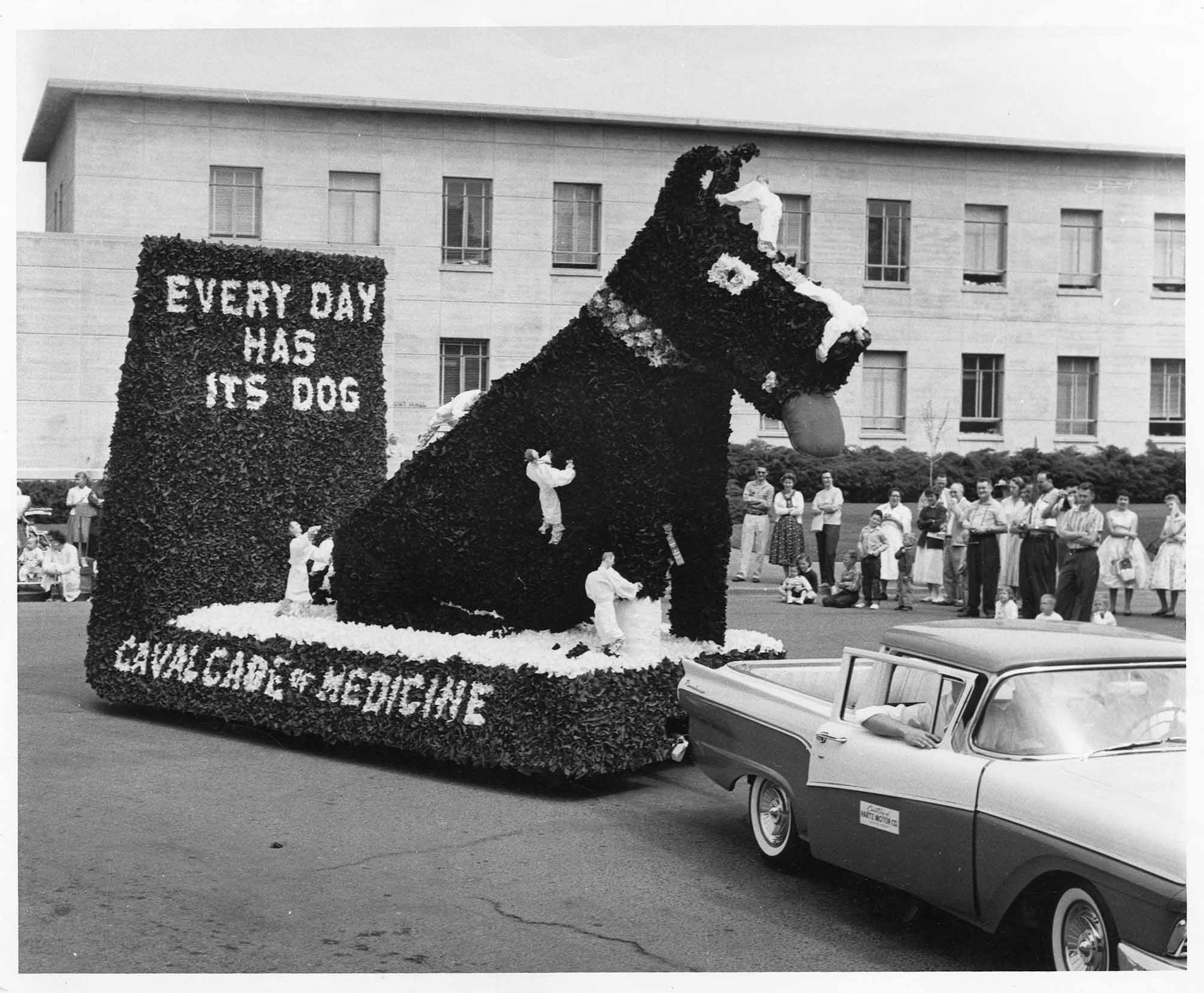 Black and white photo of parade float with dog and text: Every day has its dog