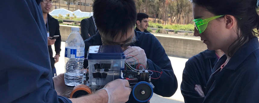 Two students closely examine wires around a miniature car