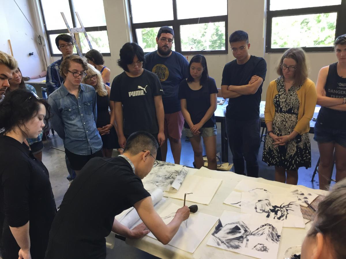 Students stand around an ink brush demonstration in class. 