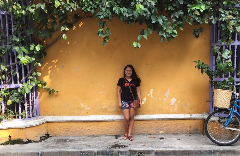 Cindy poses against a yellow wall with vines - linguistics major