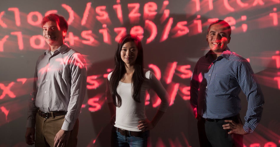 Ashley Han, a science and technology major, stands with professors Colin Milburn (left), incoming chair of the Science and Technology Department, and Gerardo Con Diaz of the Science and Technology Department.  They stand in red computer code because the work that Han and Diaz have been doing is on computer programs.