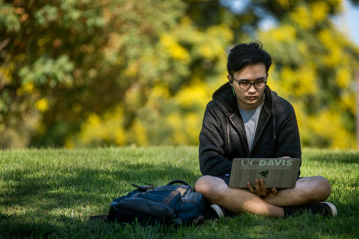 A student works on the lawn with his legs crossed. 