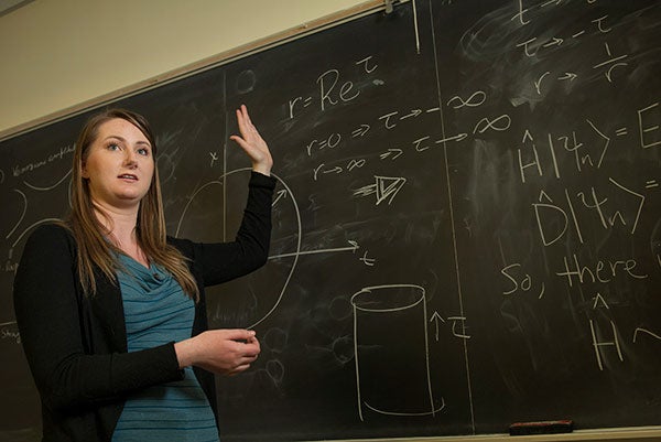 Rachel Houtz lecturing in front of a black board with physics information