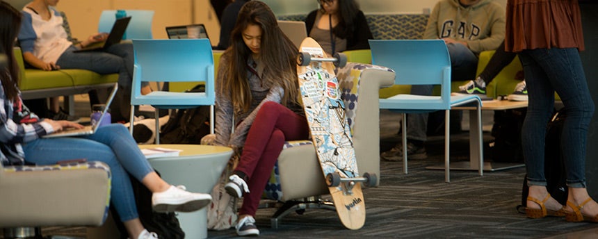 Female student sitting in the Coffee House with her skateboard