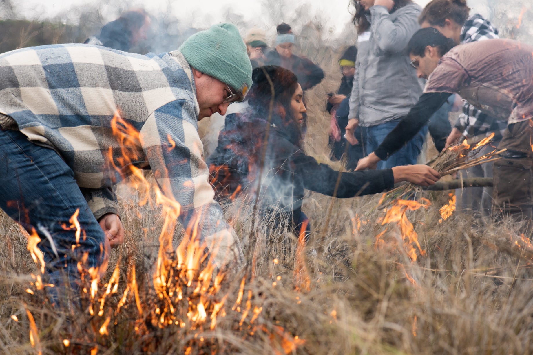 Men and women in jackets light field of deergrass on fire as part of cultural burn in California.