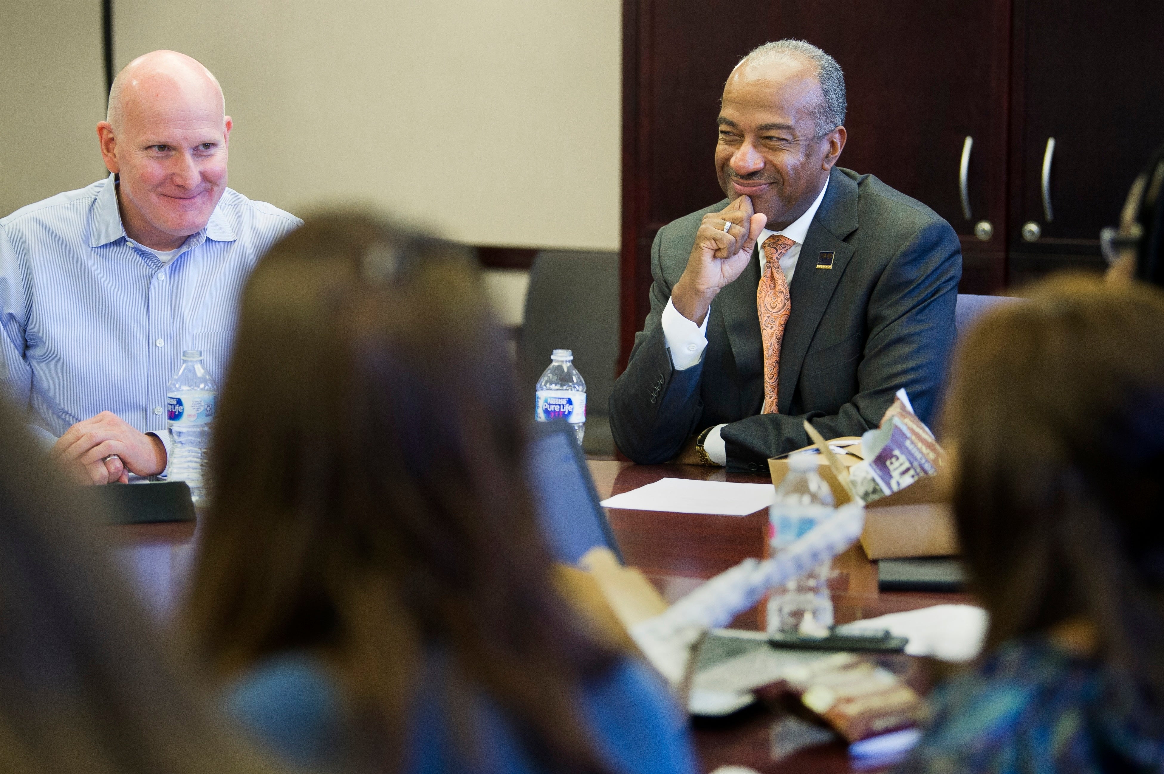 Two men smiling at a conference table, photo; blurred attendees in foreground