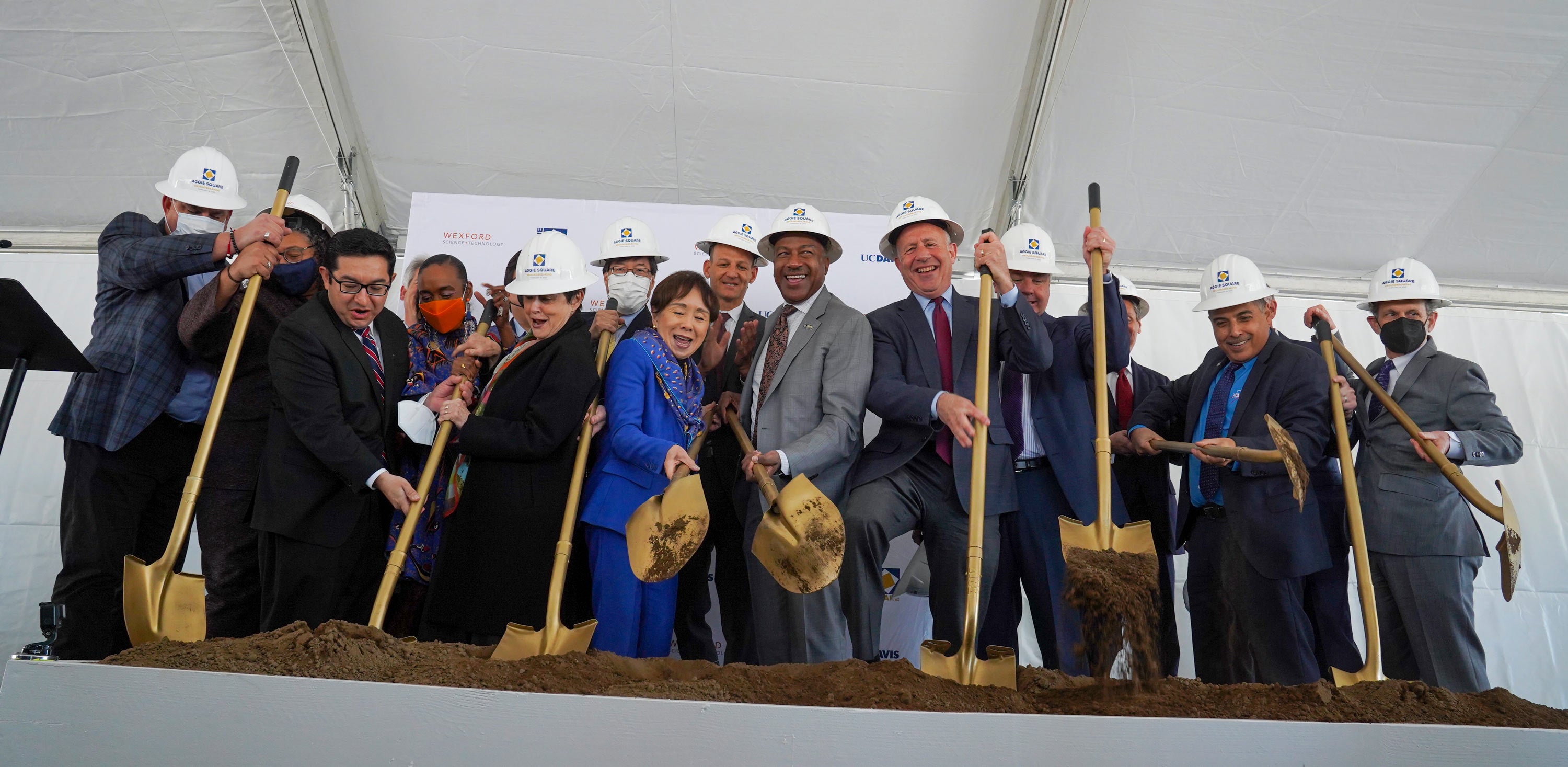 for ceremoniaLong line of executives in hard hats and wielding gold shovels l groundbreaking