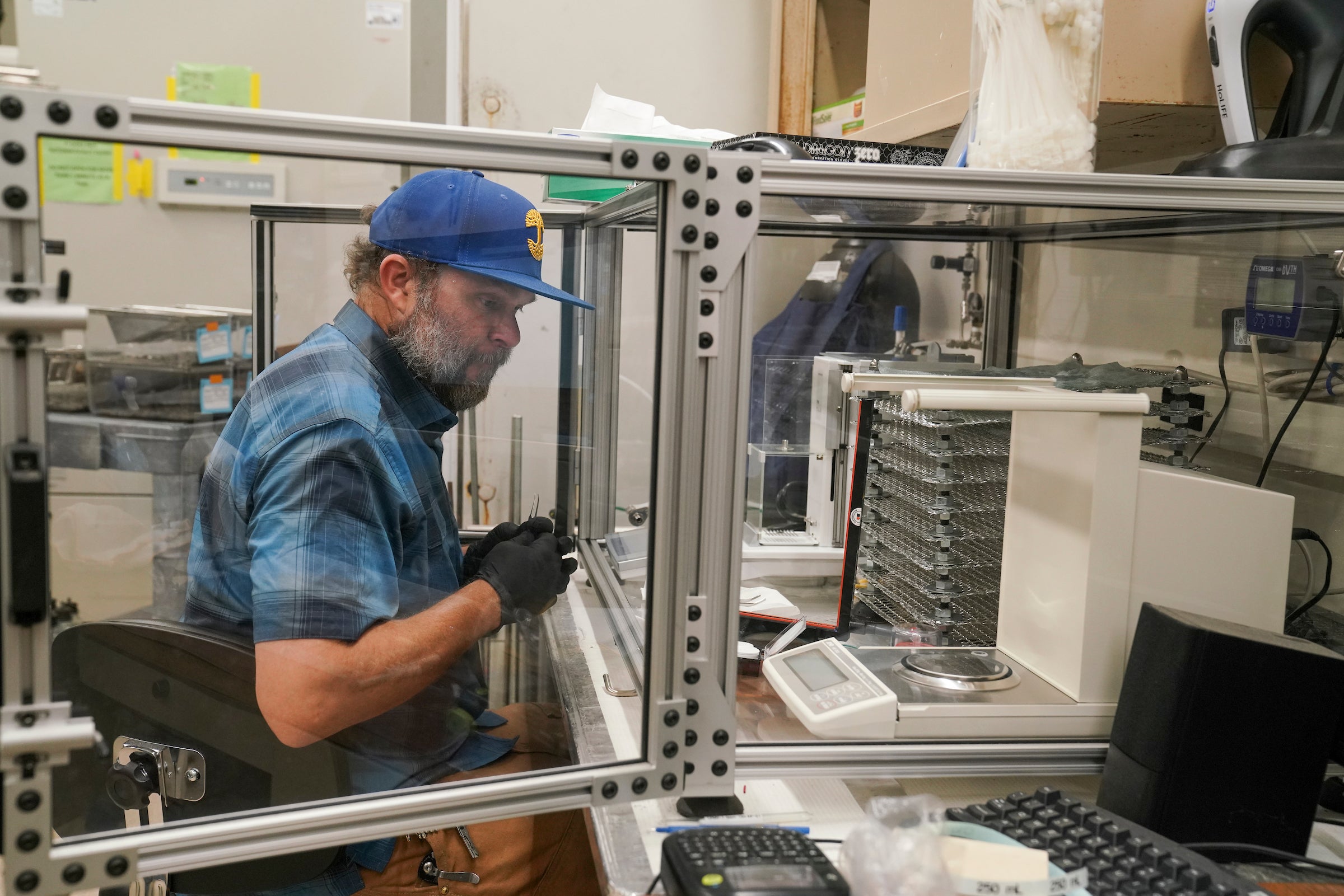 Man in blue shirt and cap seated in lab at work on airquality research