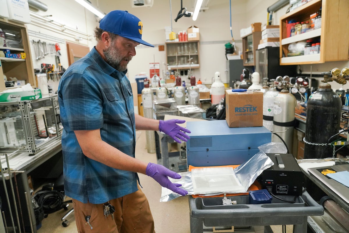 Man in blue hat and shirt in lab looks at screen of air pollution samples in lab