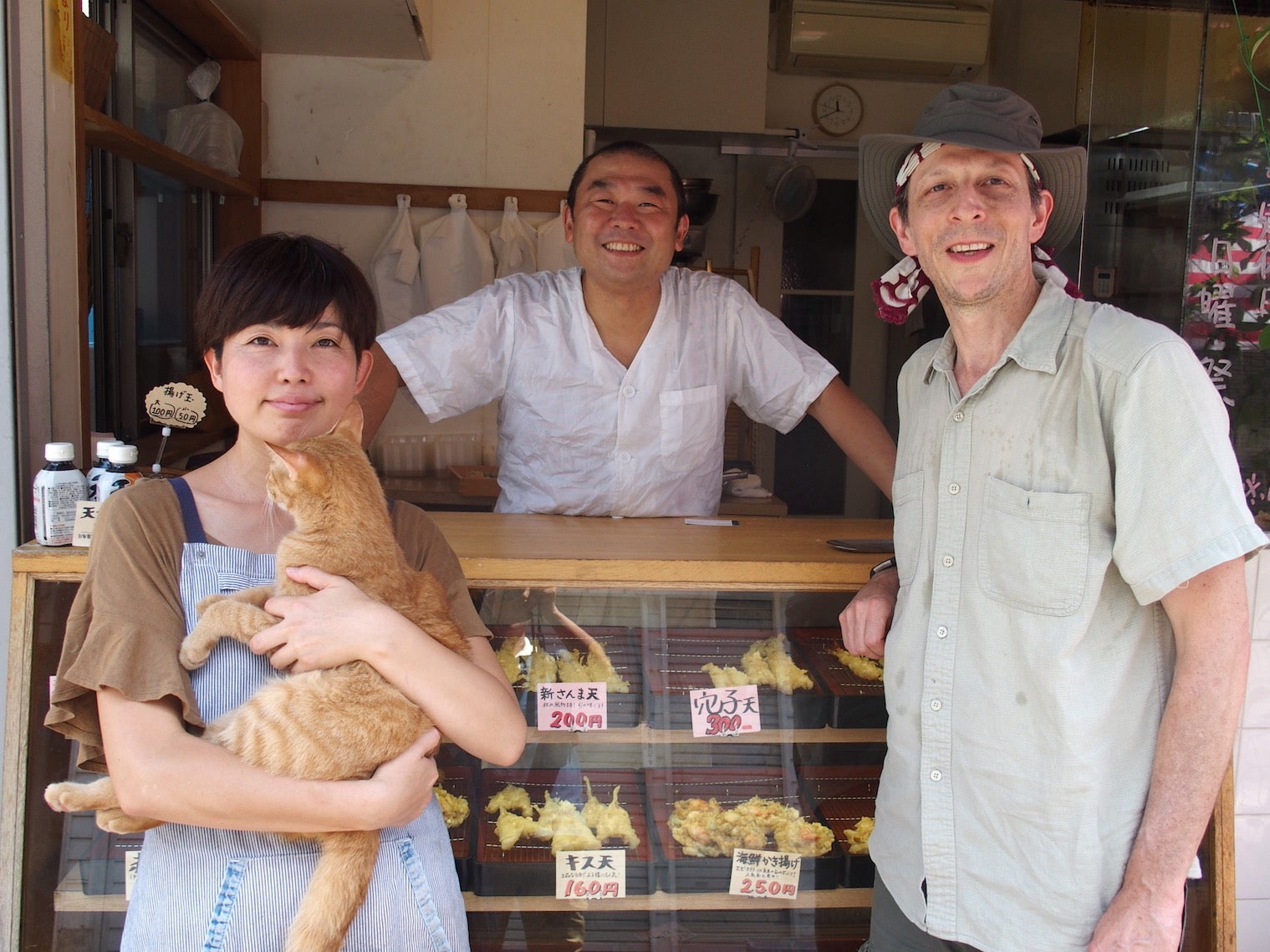 A professor poses with a shopkeeper holding a cat. 