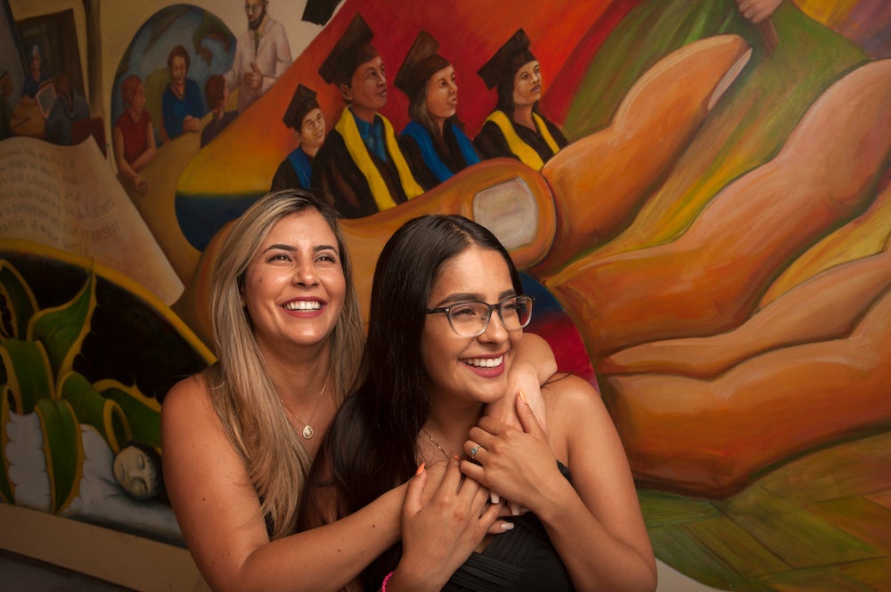 A mother and daughter smile in front of a mural. 
