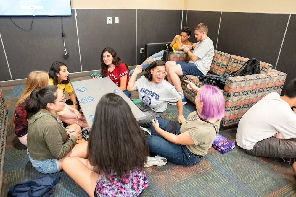 Students laugh around a coffee table inside a dorm at UC Davis. 