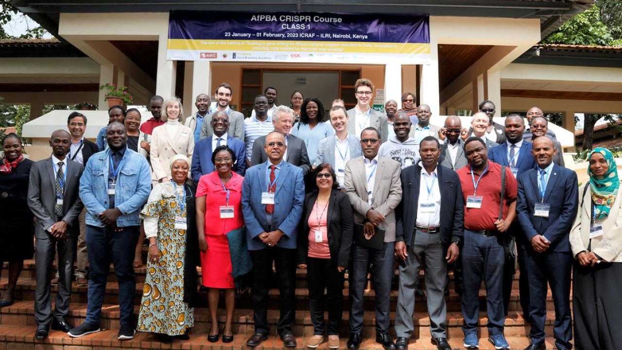 A group of men and women in a formal class portrait outdoors on the steps of a building. Most of the people are black. A sign behind them reads "AfPBA CRISPR Course Class 1 23 January - 01 February 2023 ICRAF-ILRI, Nairobi, Kenya"