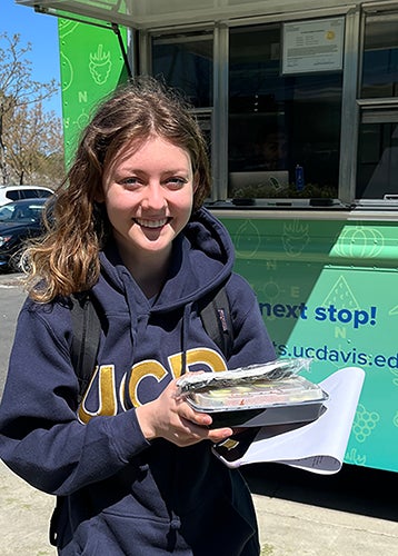 Alexandra Sarimsakci holding a meal in front of the order window of the AggieEats food truck