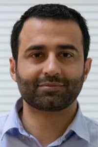 Male headshot, short dark hair and beard, light blue shirt, neutral background