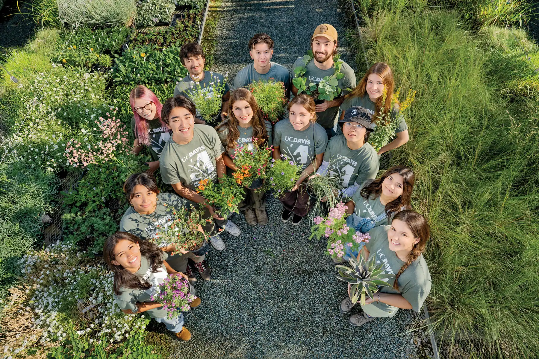 Group of diverse gardeners in a lush green garden, standing in a circle holding plants, smiling up