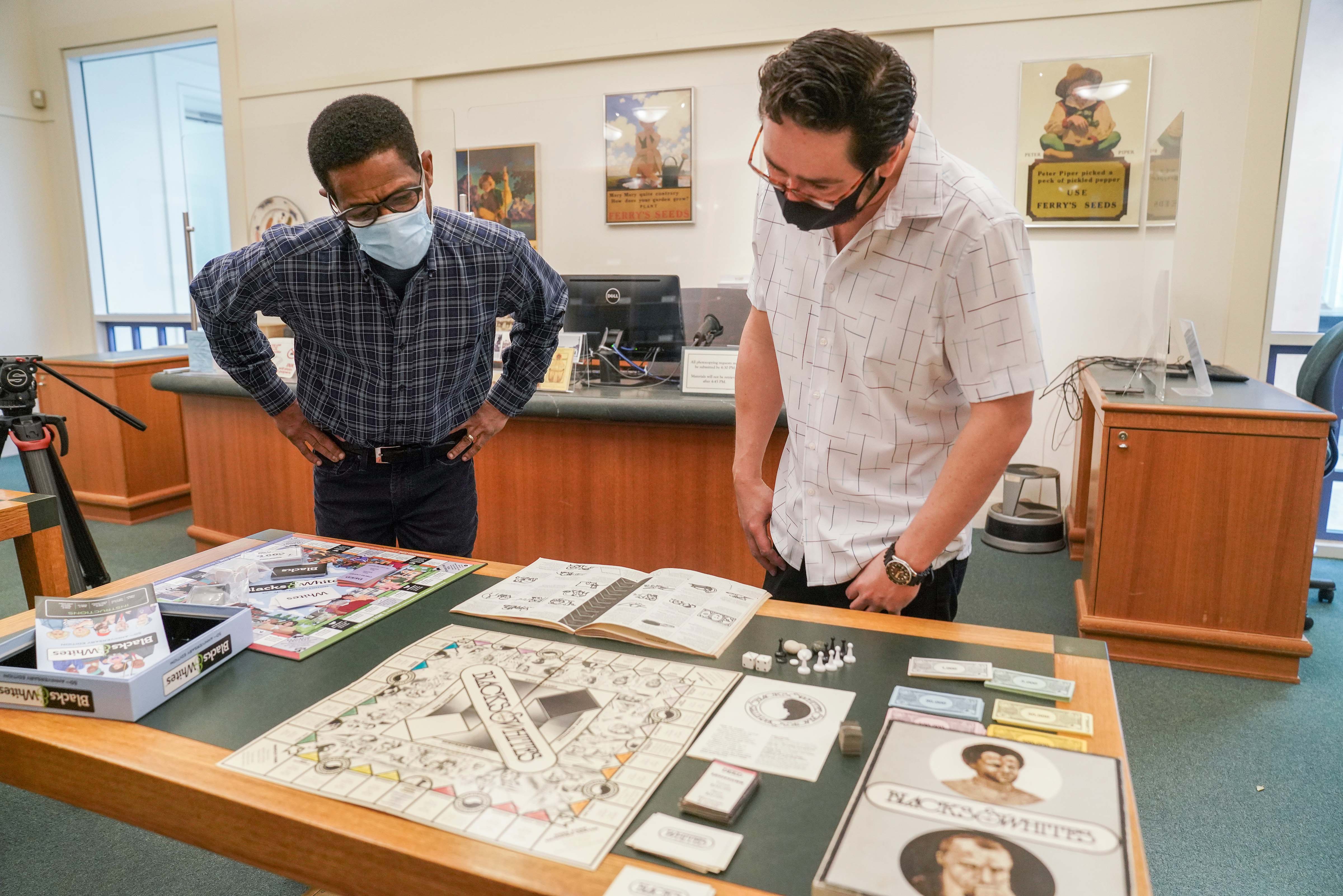 Two men look at two versions of the Blacks & Whites games that are spread out on a table