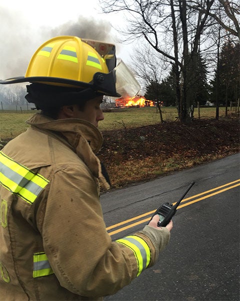 Benton Best, dressed in fire turnout, communicates by radio with a fire in the background