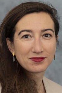 Headshot portrait of a woman with long brown hair, red lipstick, and small gold pearl earrings