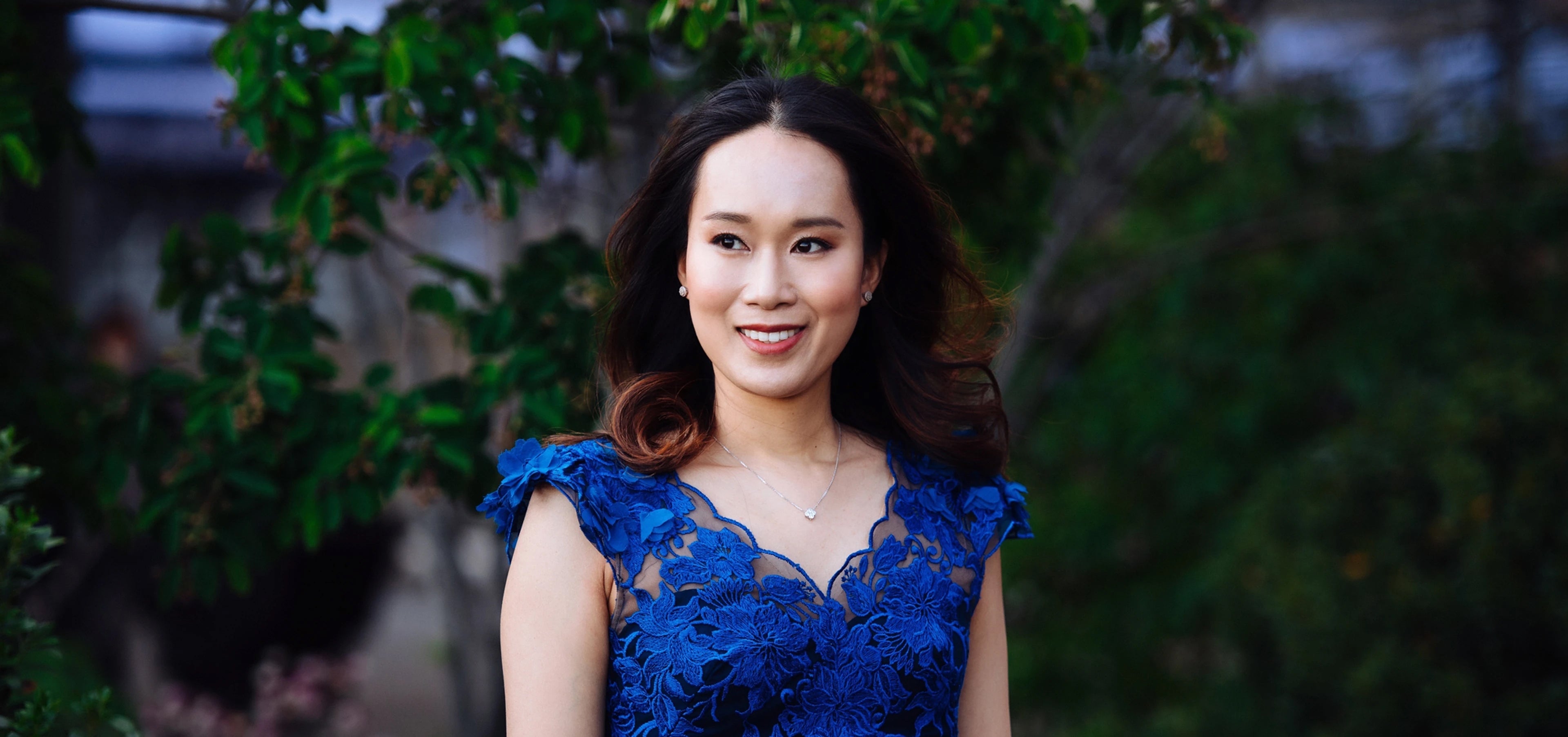 Woman wearing blue dress on, greenery in background