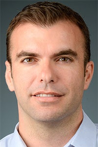 Headshot of smiling man with short brown hair and light blue shirt against gray background