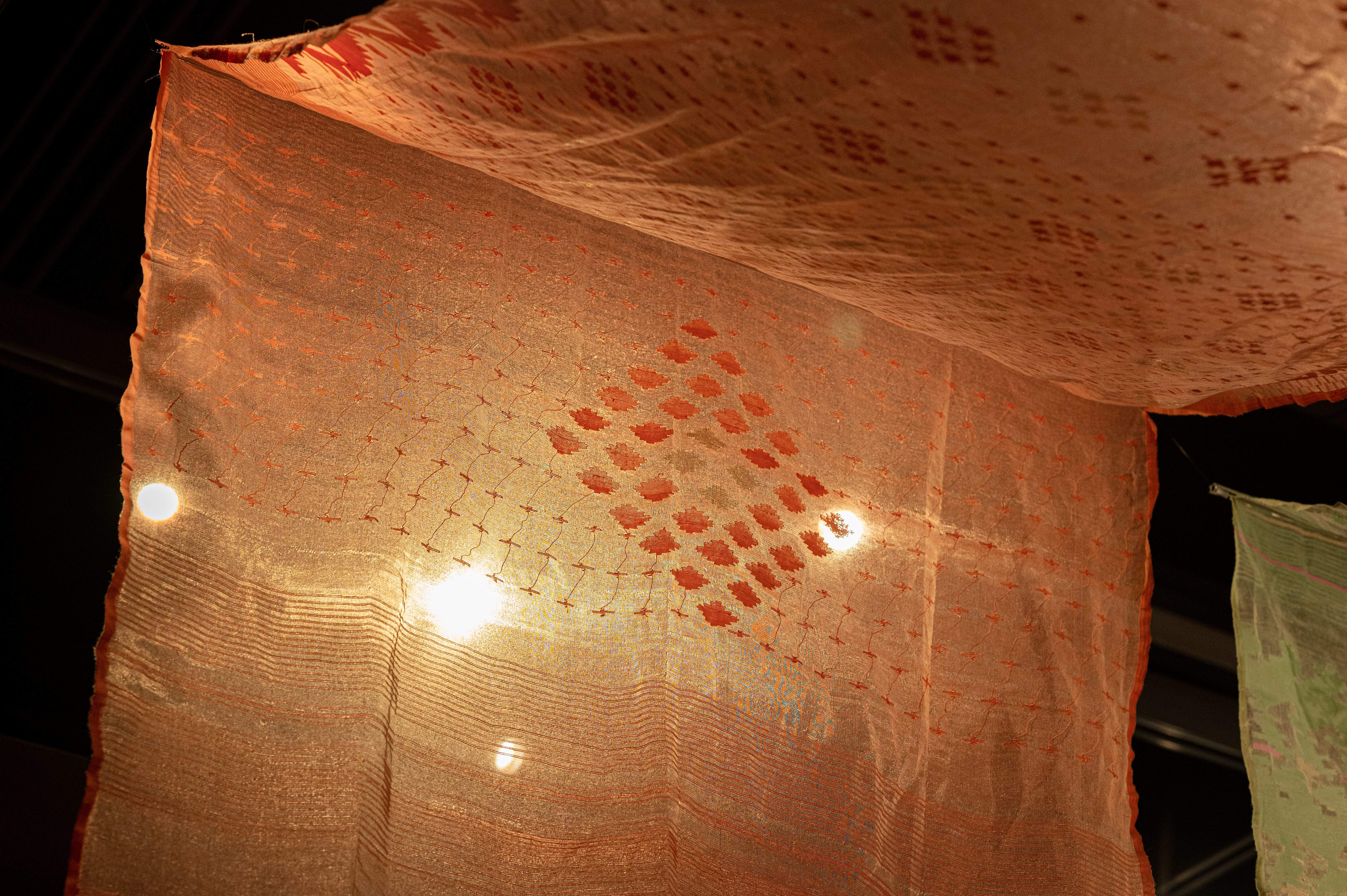 Close up of a coral Jamdani. Small red diamonds in the shape of a larger diamond are woven into the center of the fabric.