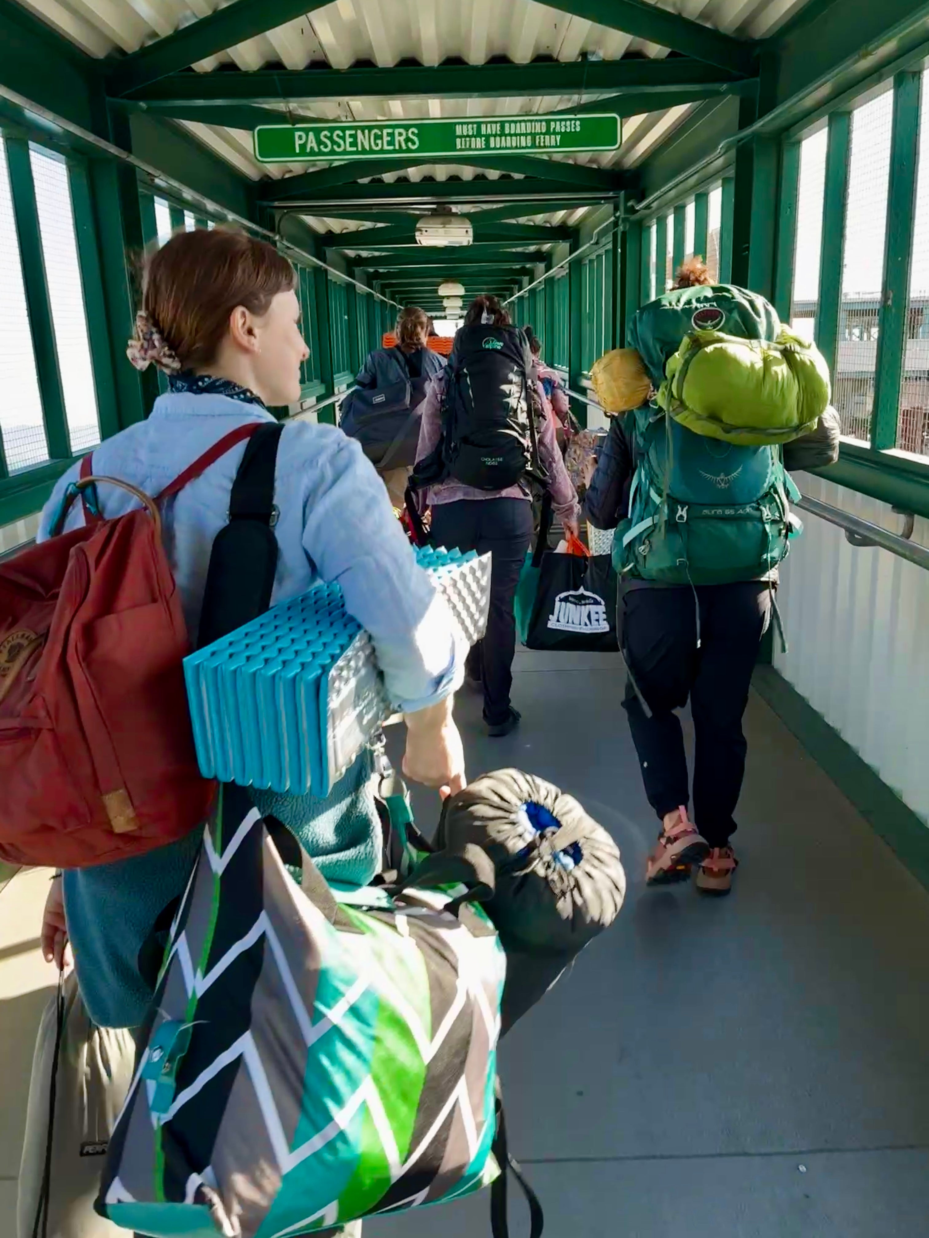 Passengers walking through covered green walkway carrying backpacks and luggage