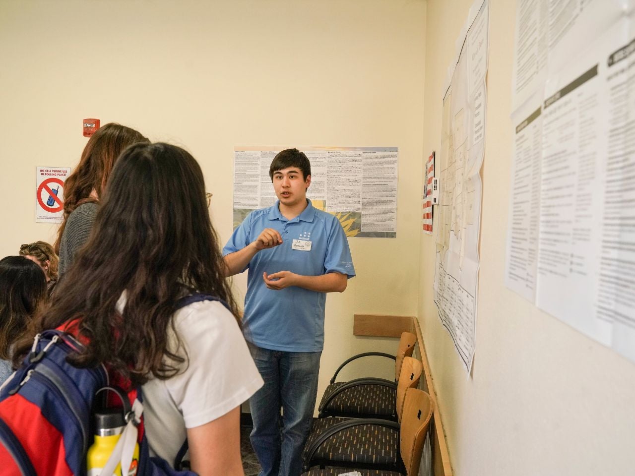 UC Davis political science major Francois Kaepellin stands in front of a wall covered in informational posters, speaking seriously to a pair of students.