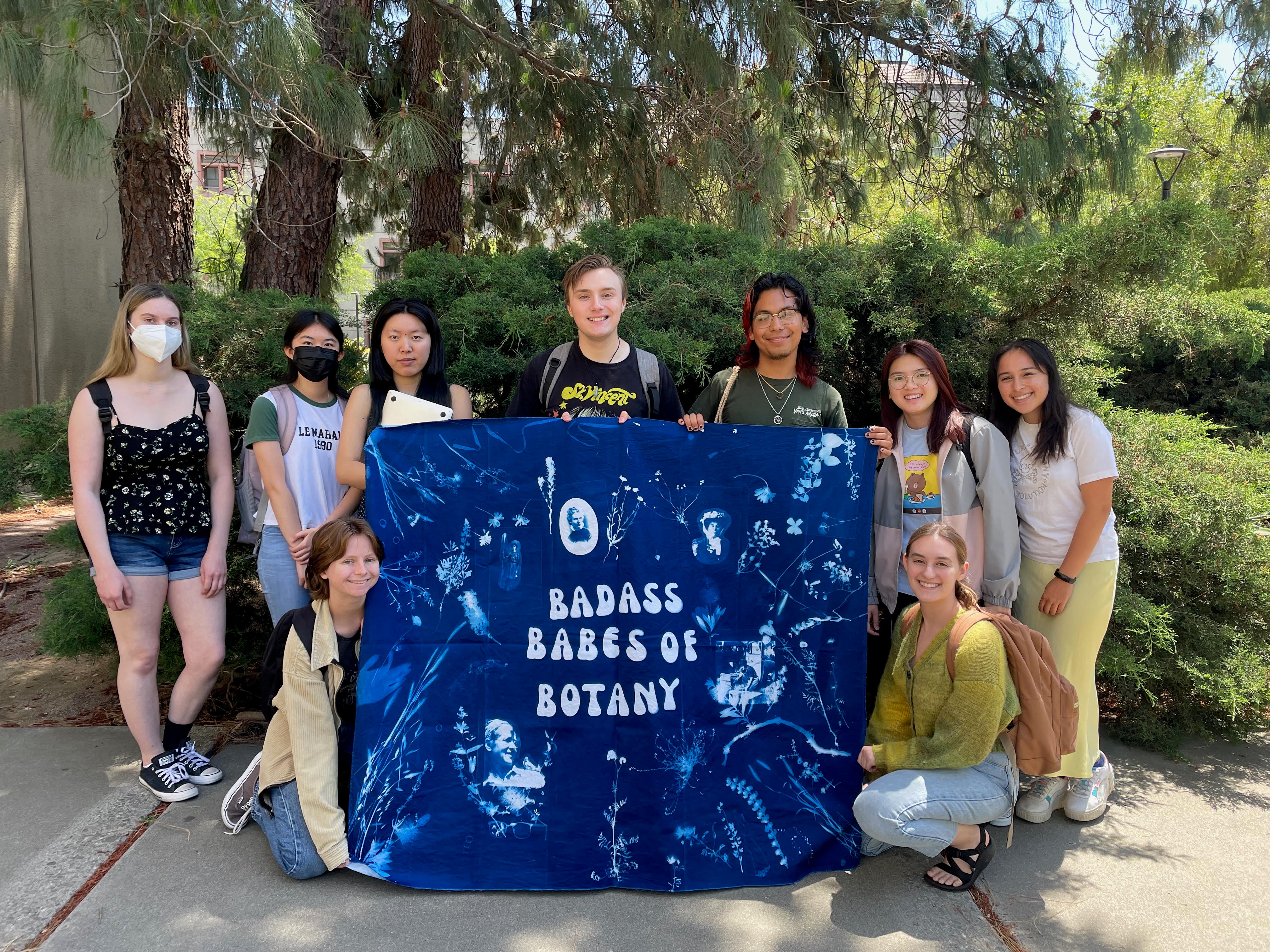 Undergraduates pose with a large fabric poster reading "Badass Babes of Botany"