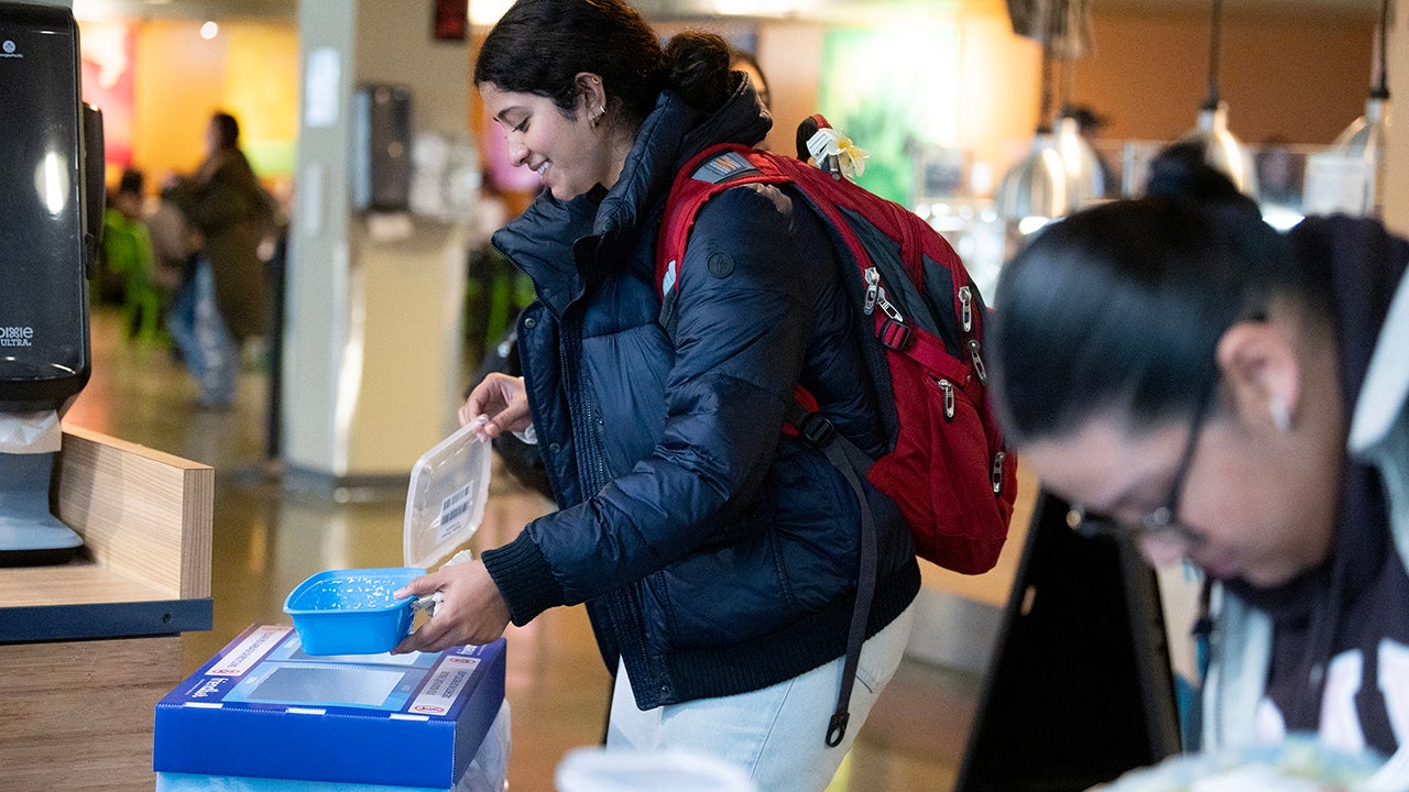 A student deposits a reusable container into a bin for pick up and washing.
