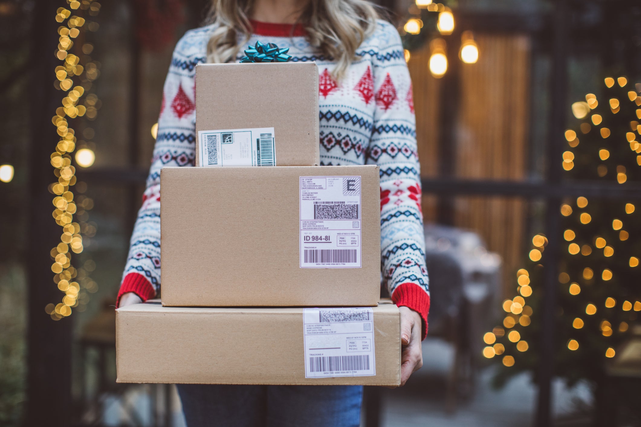 Female caucasian in holiday sweater holds three stacked shipping boxes