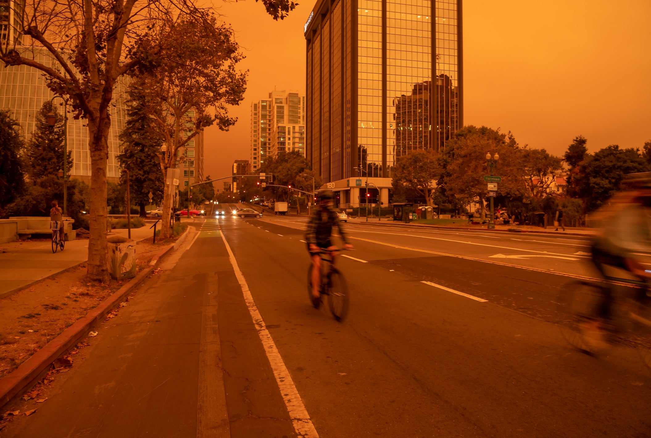 orange sky from wildfire smoke over Oakland California street with cyclist and buildings in background