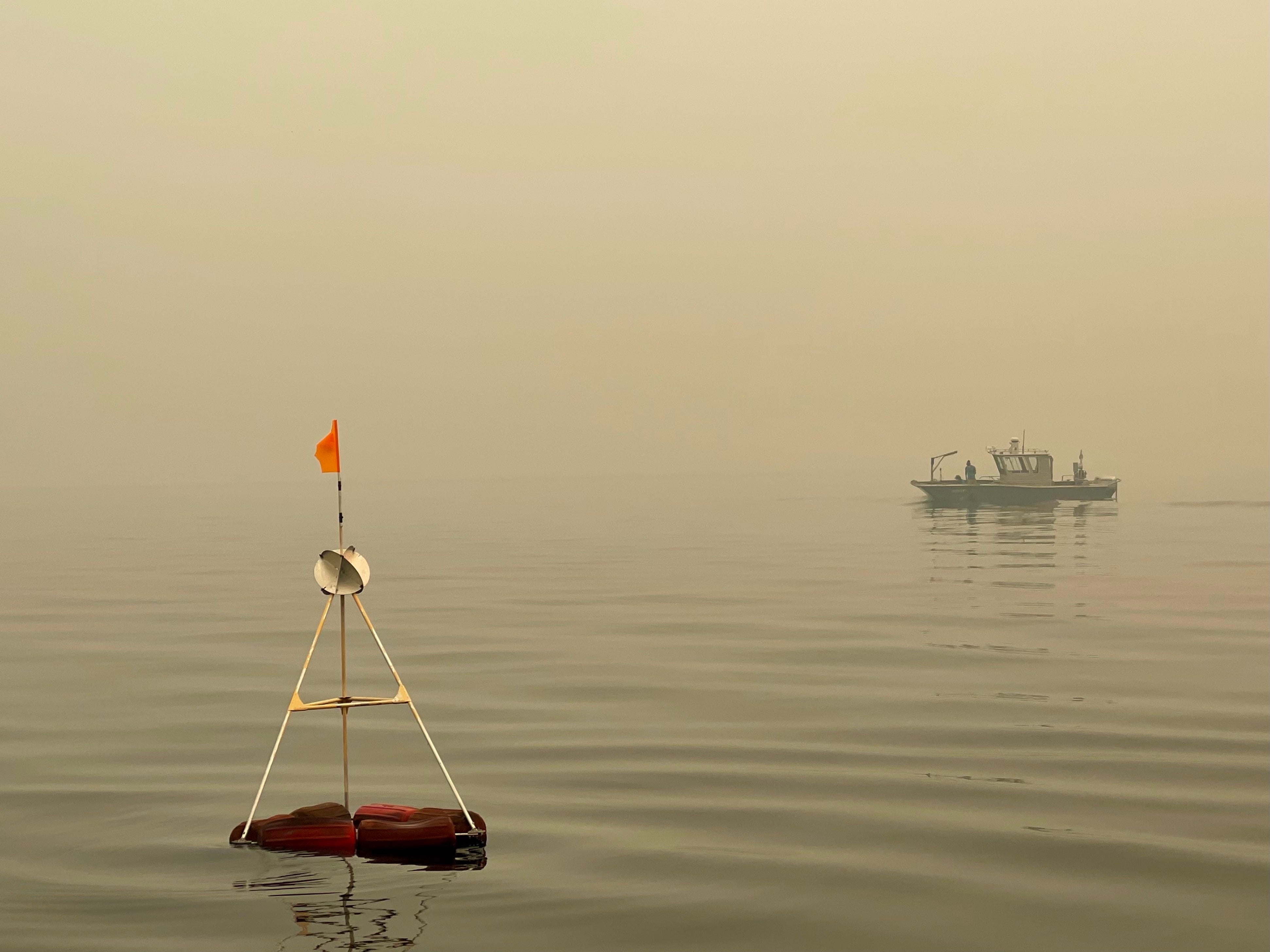 A buoy in Lake Tahoe with boat in the background under smoky skies
