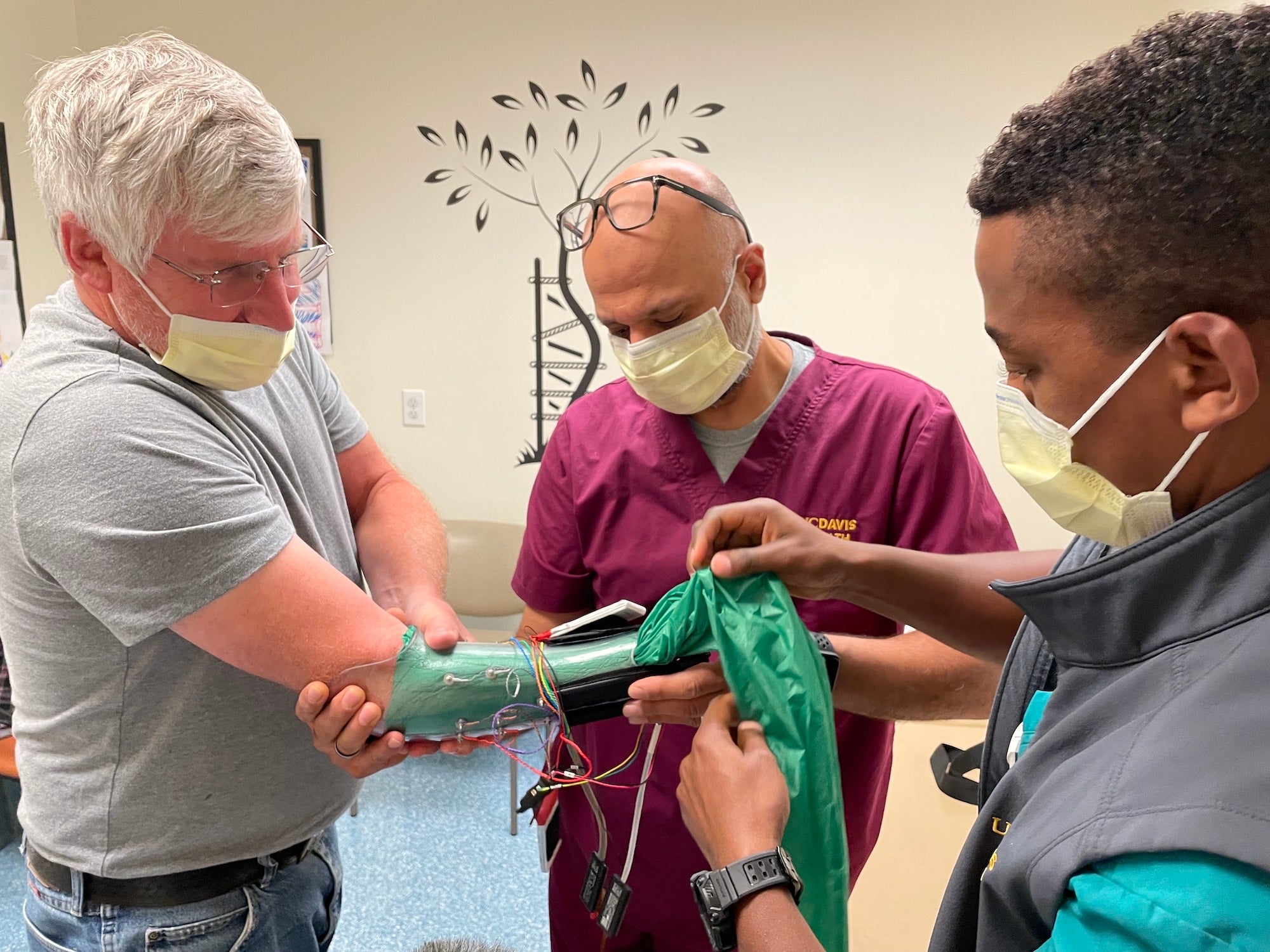 David Brockman puts his arm into a carbon fiber sleeve that will attach to his prosthetic hand. Fehran Maher and Laduan Smedley, both certified prosthetists, help him with the fitting.