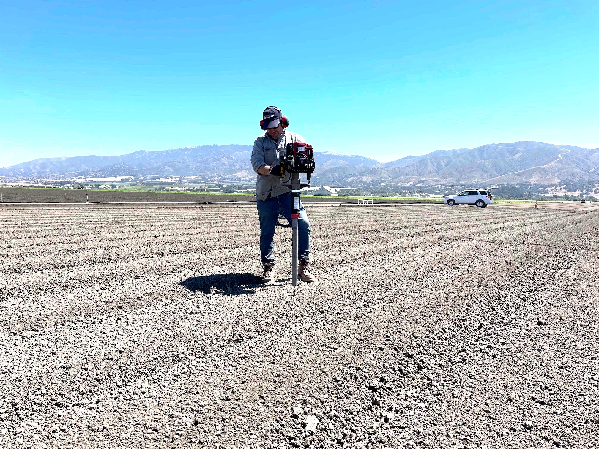Cole Smith of UC Davis walking on plowed field carrying gear in front of mountains under a clear blue sky