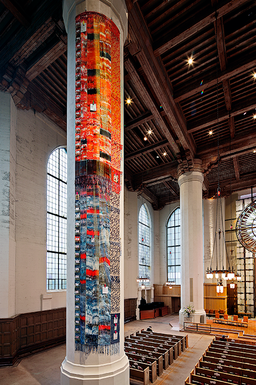 Tall tiled mosaic column in a light-filled church nave with wooden beams and pews