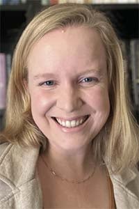 Portrait photograph of a smiling blonde woman, bookshelf background
