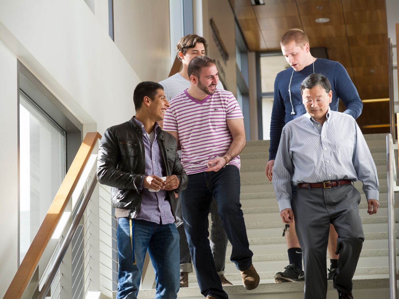 A group of four students and UC Davis School of Law Professor Clay Tanaka laugh and converse while descending the stairs in King Hall.