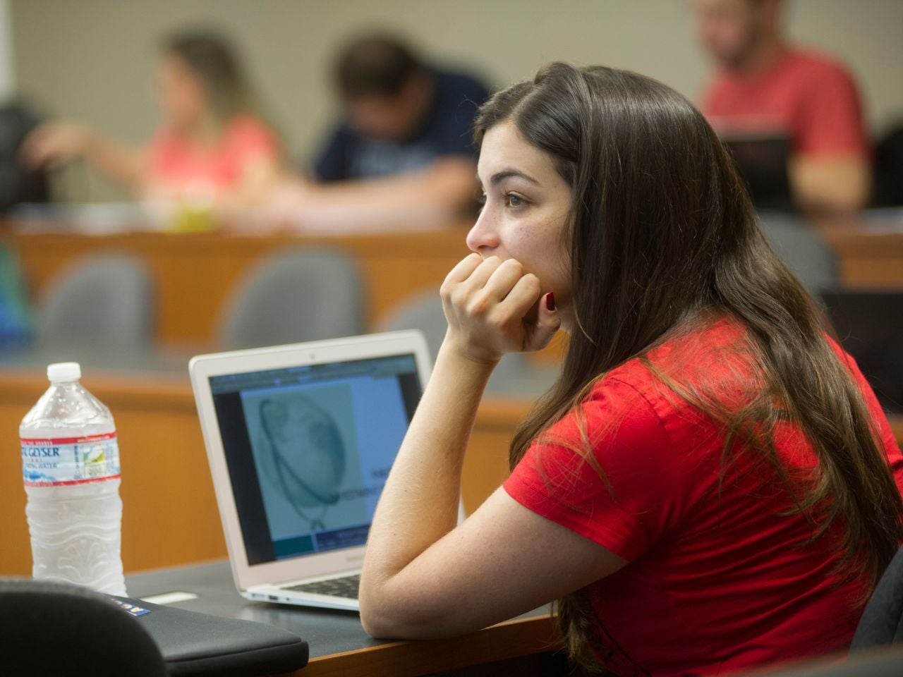 A student sitting in class at King Hall stares off in thought with her chin propped on her hand, laptop open in front of her.