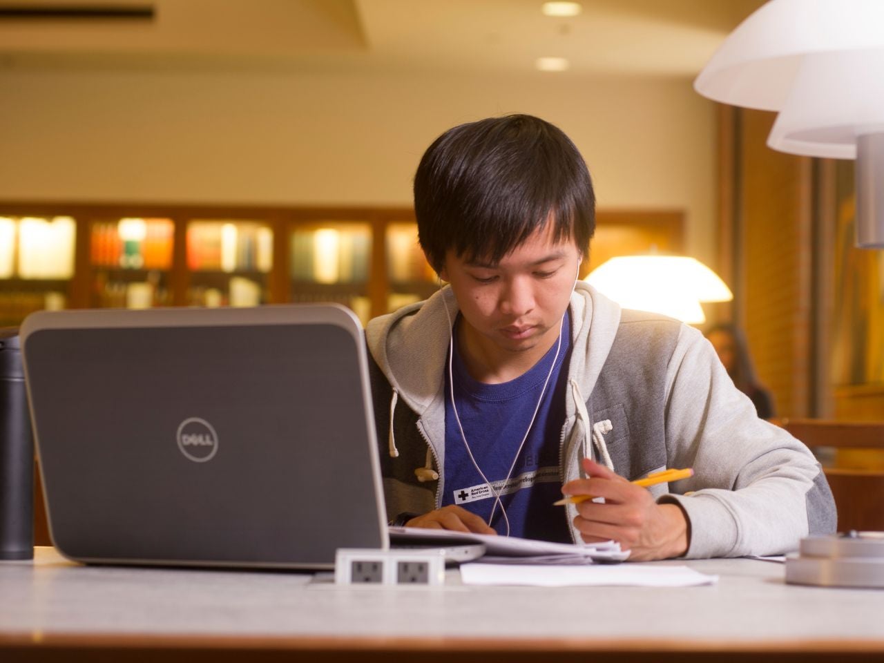 A student sits poised to write on a piece of paper in front of a laptop in Mabie Law Library.