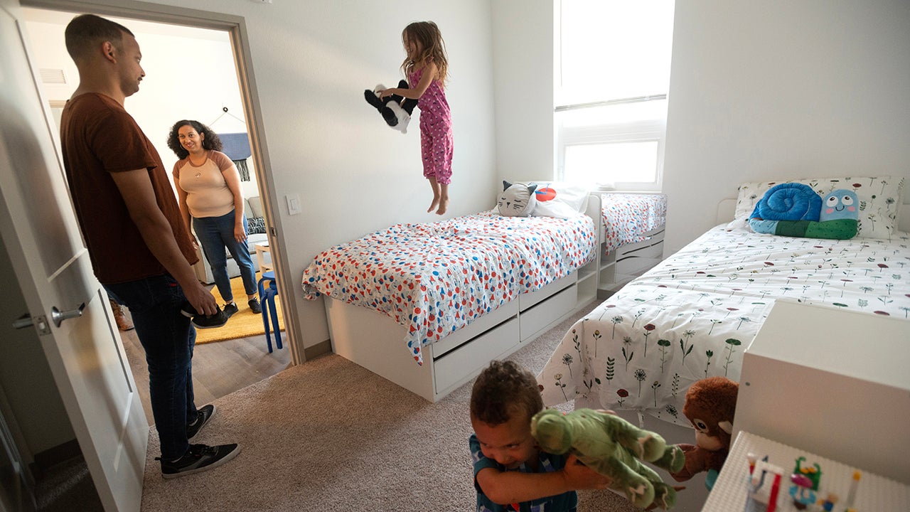 Parents look on as their daughter hops on a bed in an apartment at Orchard ParkA girl hops on a bed as her parents look