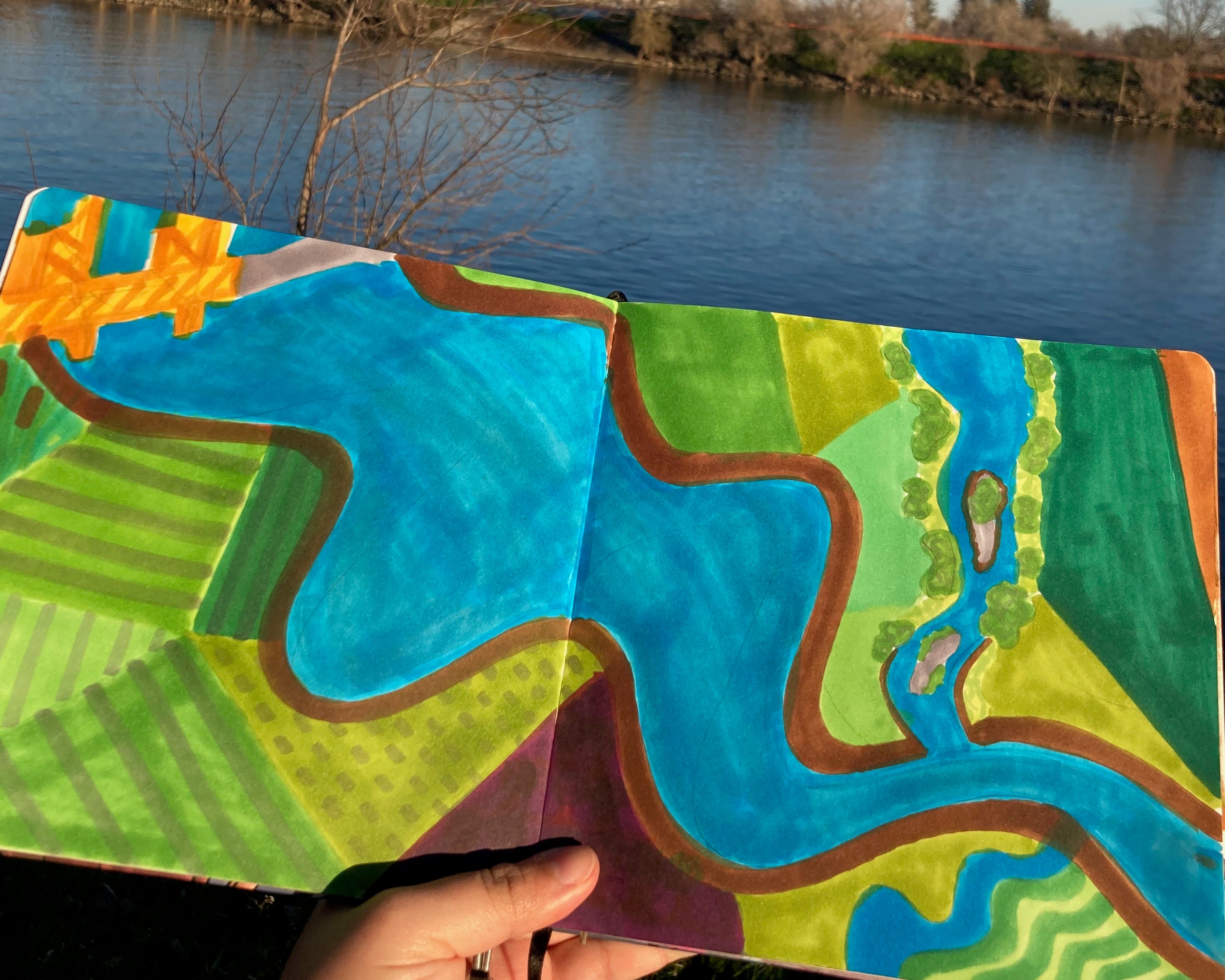 painting of river in sketchbook held up by hand with Sacramento River in background