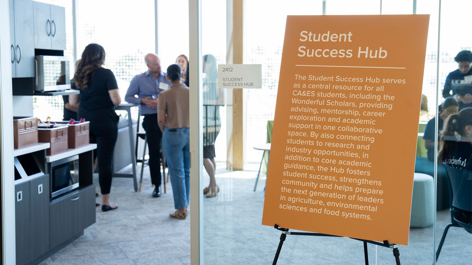 Student Success Hub orange signboard and students talking in bright modern lounge