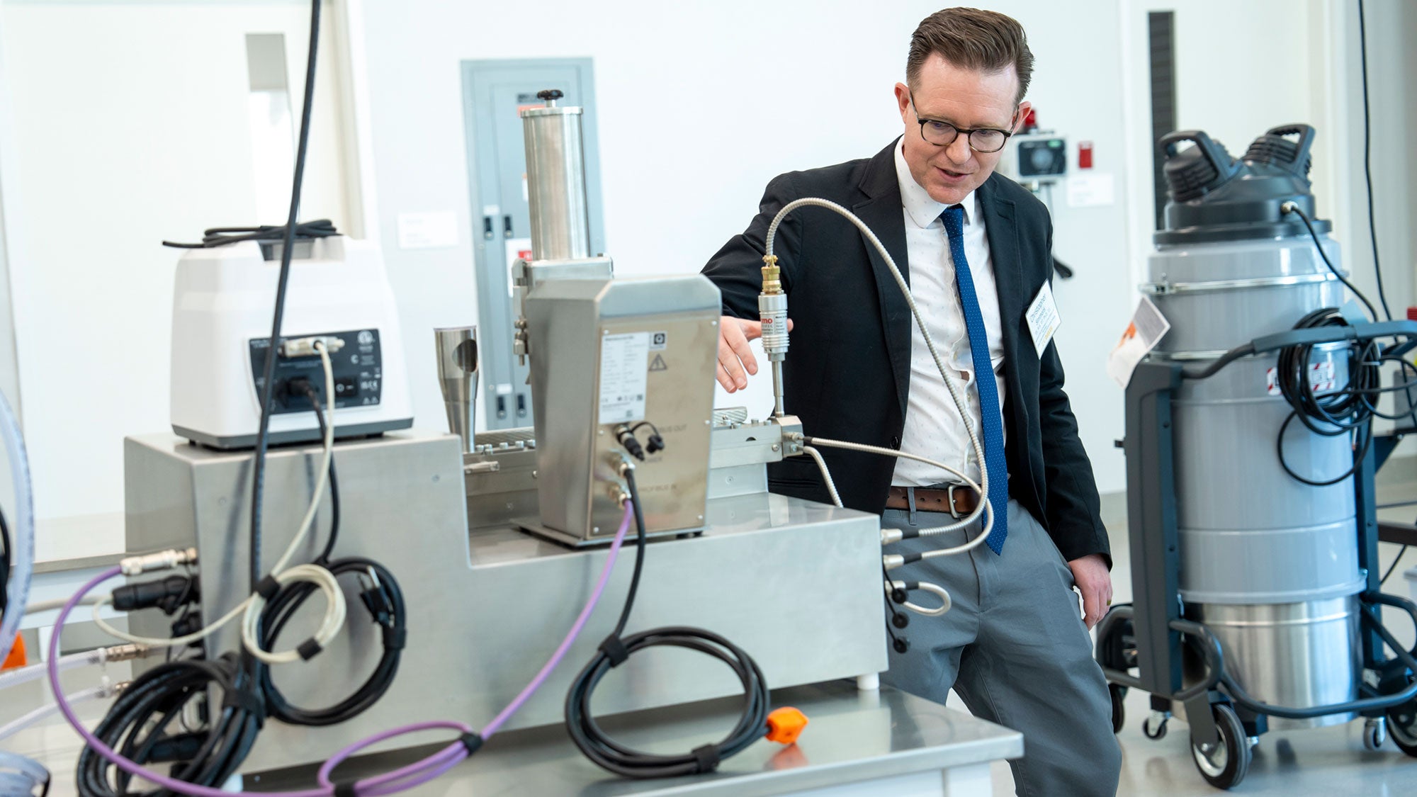 Man in suit and glasses inspecting machines in bright lab