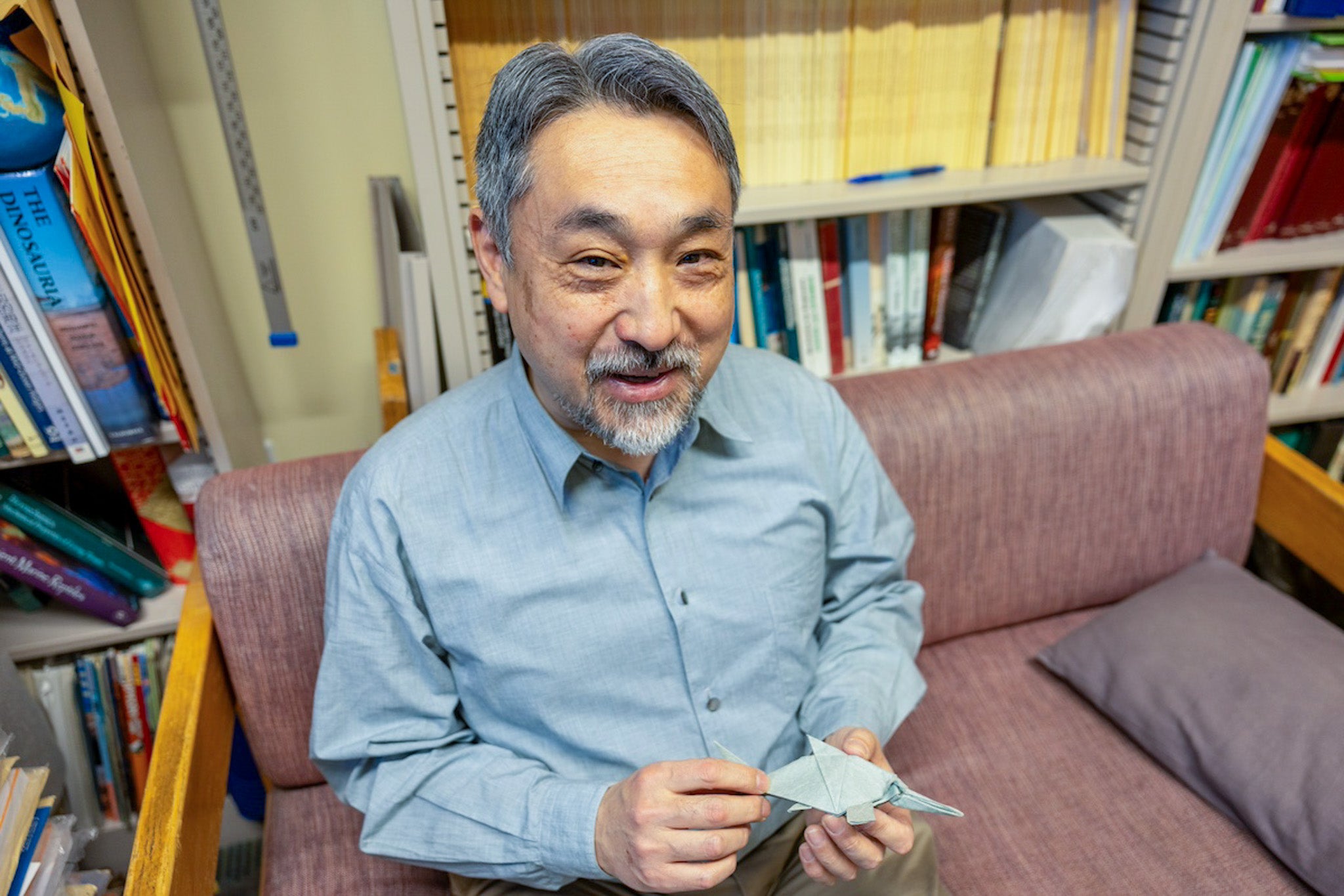 Professor Ryosuke Motania smiling on a couch in an office, holding small cards — photo
