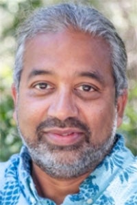 Outdoor headshot of a smiling man with gray hair and beard, blue patterned shirt