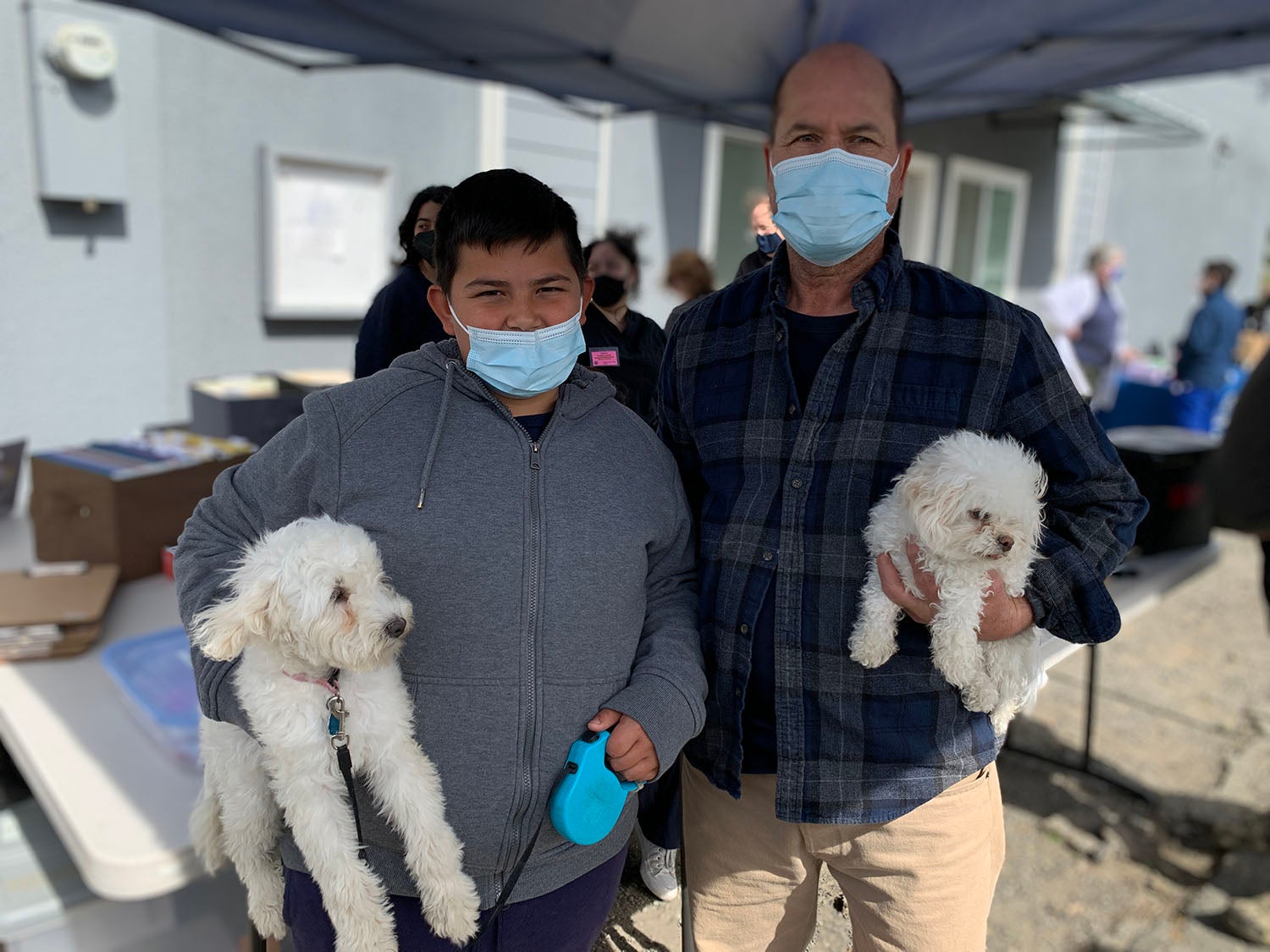 Santos Lopez, right and his son Johnathon, left, hold their little white poodle mixes that they brought for vaccinations at the Knights Landing One Health Clinic.