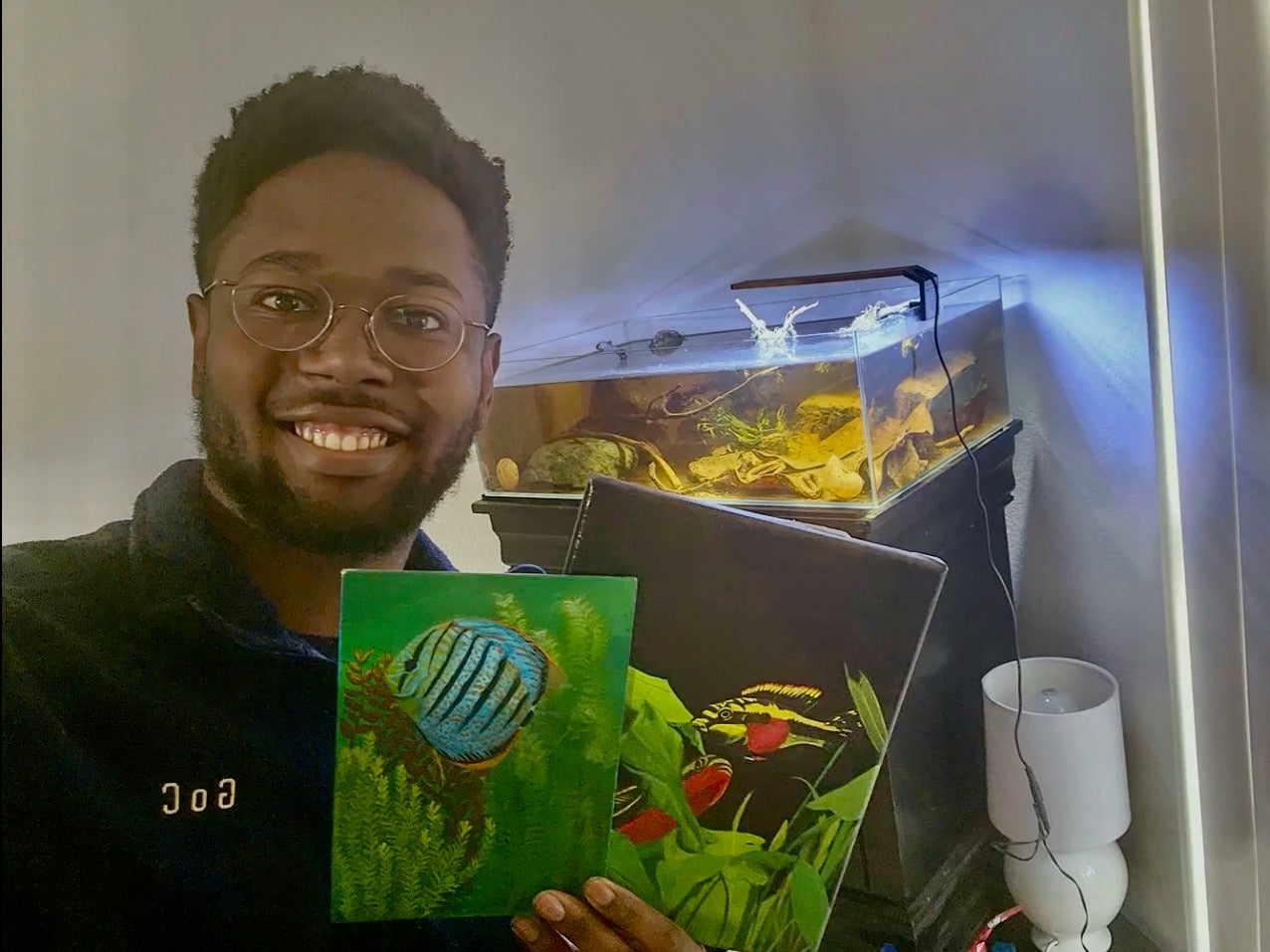 Khalil Russell smiles while holding photos of fish in front of fish tank.