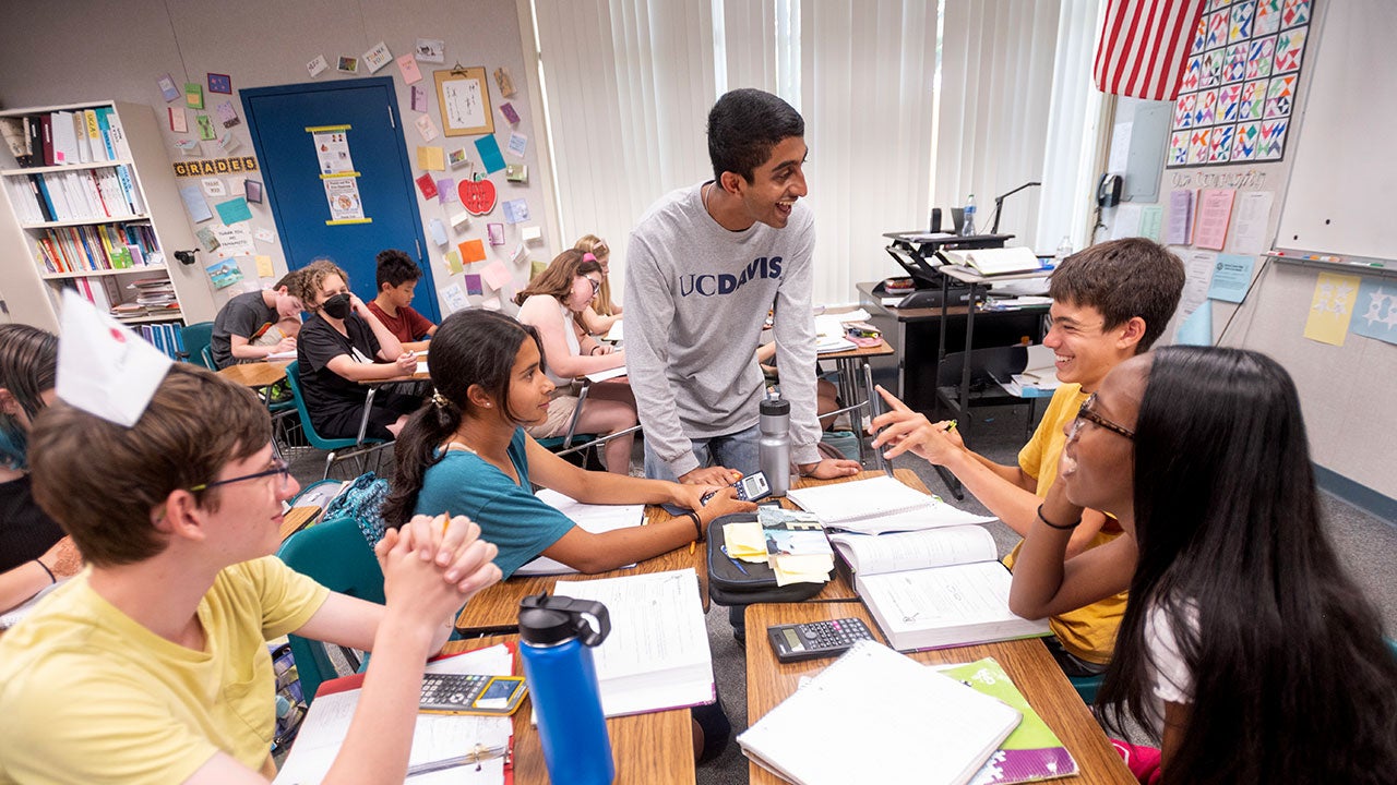 Stading, Neeraj Senthil talks with four seventh grade students seated at desks